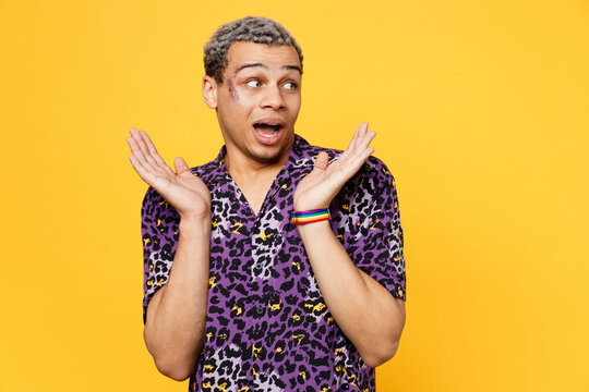 Young Surprised Amazed Shocked Gay Man Wear Purple Animal Print Shirt Look Aside On Area Spread Hands Isolated On Bright Plain Yellow Color Background Studio Portrait. Lifestyle Lgbtq Pride Concept