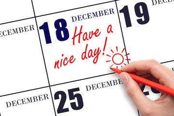 The hand writing the text Have a nice day and drawing the sun on the calendar date December 18