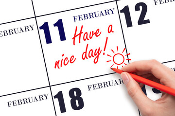 The hand writing the text Have a nice day and drawing the sun on the calendar date February 11