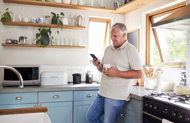 Coffee, phone and elderly man in kitchen texting and reading news or social media in his home....