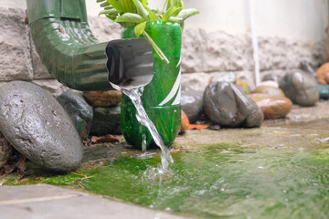 Rain water is pouring from the green draining gutter on the mossy ground, selective focus