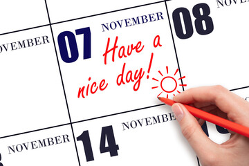 The hand writing the text Have a nice day and drawing the sun on the calendar date November 7