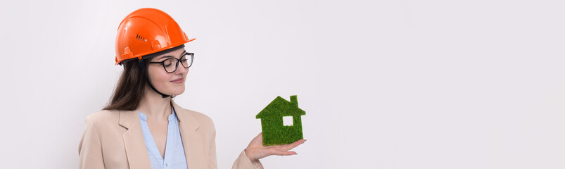 A girl in a construction helmet holds a green house. The concept of ecological clean housing.
