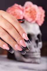 Hand with long artificial manicured nails colored with black nail polish and scull with flower...