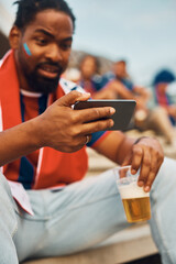 Close up of black sports fan watching football match on cell phone.