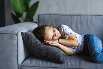 Close up little girl taking day nap, sleeping on cozy comfortable couch at home, cute adorable kid child with closed eyes lying resting on sofa, enjoying healthy sleep, falling asleep alone