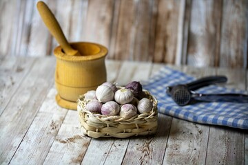 Basket of small garlic on a wooden kitchen table with a mortar and a pestle