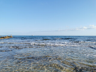 The coast of the Mediterranean Sea, a stone ridge, at the end of which is a fisherman, in the sea a white pleasure yacht against a blue sky with clouds.