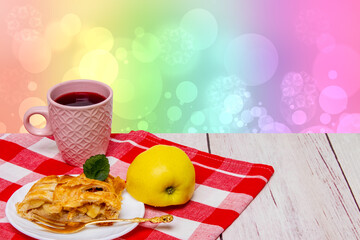 A slice of homemade baked fresh apple strudel with a cup of coffee and a fresh apple on red picnic cloth over abstract spring background. Concept morning coffee. Space.