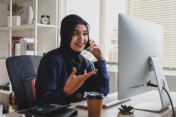 Muslim business woman working with computer at office, having business conversation on mobile phone