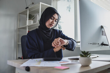 Muslim businesswoman working with computer while sitting at the table in an office and looking at...
