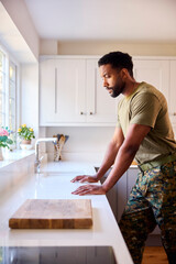 Thoughtful Male American Soldier In Uniform In Kitchen On Home Leave Looking Out Of Window