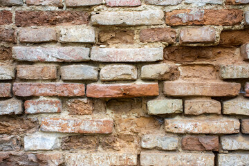 Old ancient brick wall with protruding bricks in brown and red tones, holes in the wall, fallen bricks and crumbling cement, symbolizing antiquity and the change of generations. For use as background
