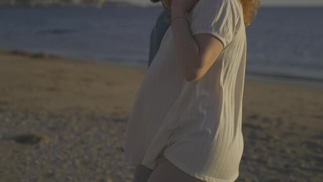 Pregnant Couple walking along sandy beach in front of ocean at sunset time