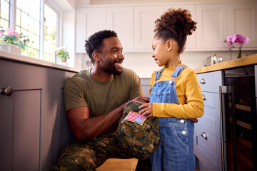 Daughter Holding Cap Of American Army Father In Uniform Home On Leave In Family Kitchen