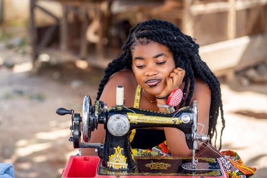 image of african lady sitting in front of sewing machine with the hand at the chin- 