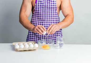 Chef bodybuilder in protective apron and cook eggs on whie kitchen table. Muscular man cooking. Healthy food and dieting. Food additives for sportsman, daily calorie diet