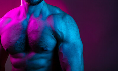 Sportive man bodybuilder is posing in the colorful neon light with naked muscular torso showing...