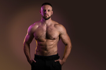Fototapeta na wymiar Portrait of a handsome muscular bodybuilder posing over warm dark background. Naked muscular torso, chest, biceps and abs