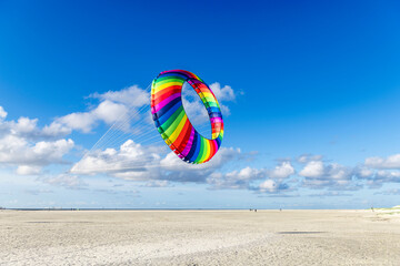 Round rainbow kite above the wide sandy beach