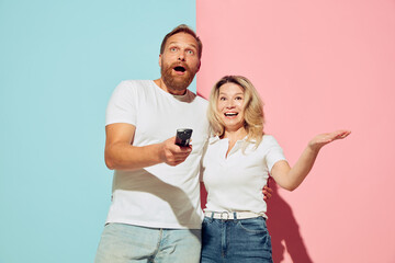 Expressive young people, man and woman, husband and wife spending time together isolated over blue and pink background.