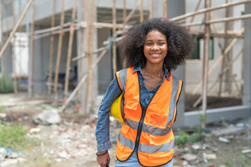 Fototapeta premium Portrait of Young female African American civil engineer wearing safety vest and hold yellow helmet standing at housing estate construction site