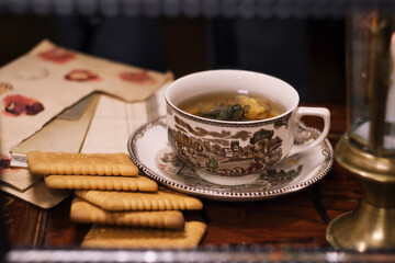 Holiday evening at home - porcelain cup of best herbal tea, antique candle in candlestick, old letters and jar of honey