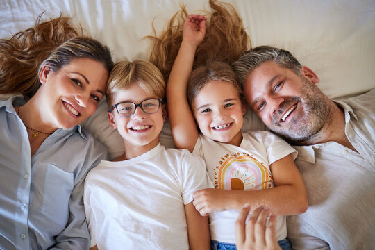 Top view, family or children bonding in bedroom in house, home or hotel and parents in trust, love or security. Portrait, smile or happy kids with mature father and mother or man and Australian woman