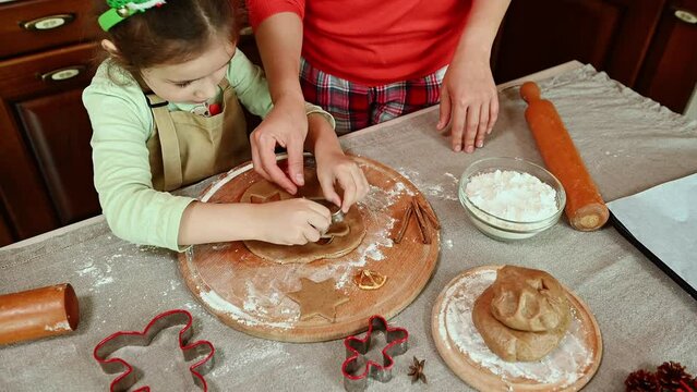 View from above of a charming little girl in an elf hoop, carving stars out of rolled gingerbread dough. Charming daughter cooks with her mother Christmas pastries in the home kitchen. Merry Christmas