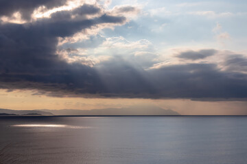 Fototapeta premium Early morning view of the sunrise over the Mediterranean Aegean Sea. View on the peninsula Mount Athos (Again Oros), Chalkidiki, Central Macedonia, Greece, Europe. Sun beams on the water surface, calm