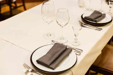 Close up new white porcelain tableware plates on purple place mats and empty wine glasses ready for dinner. Table settings wait for guests at home or restaurant.