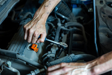 An auto mechanic works with a car engine in the mechanics' garage. Car repair close-up. An authentic close-up shot of an auto mechanic's hands.