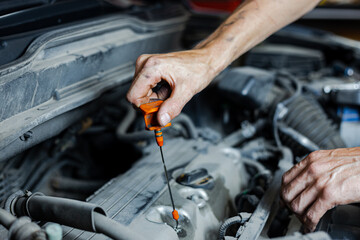 A male mechanic checks the oil level in the car engine in close-up. The mechanic holds a dipstick in his hand to check the oil level in the car.Focus on hand with yellow oil gage.