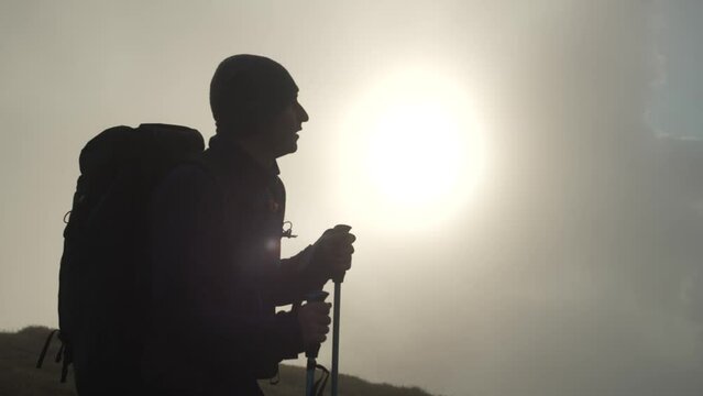 Silhouette of a male tourist with a backpack in the mountains. A man is hiking to the top of a mountain. The concept of a tortured person who goes to his dream. High quality 4k footage