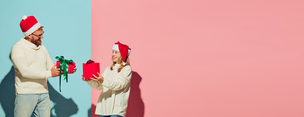 Young charming couple wearing christmas hats and white warm sweaters holding festive boxes, smiling. Romantic concept.