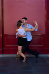 Boy in a suit and girl in shorts and a white t-shirt Couple dancing Tango, with a red background.