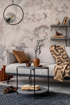 Exquisite and modern composition of living room interior with design grey sofa, rug, round pedant lamp, black coffee table, decoration, pillow and elegant accessories. Concrete grunge wall.
