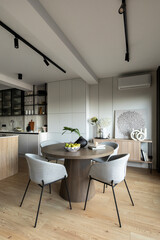 Contemporary design of dining room interior with round table, gray chairs, wooden floor, decorations, flowers in vase, paintings and elegant personal accessories. Stylish home decor. Template. 