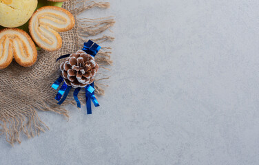 Platter of delectable cookies on a piece of cloth amid pine cones on marble background