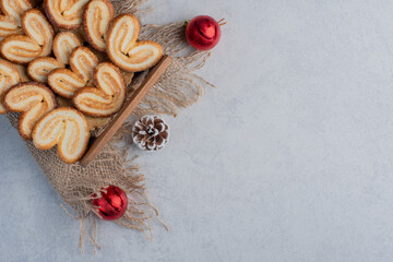 Flaky cookies piled in a wooden basket and surrounded with christmas decorations on marble background