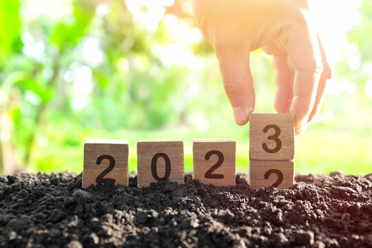 Hand changing year 2022 to 2023 in wooden blocks cubes with growing plant at sunrise. New year 2023, hope, hello and goodbye concept.
