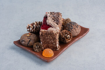 Cookies, pine cones, marmelades and a slice of cake on a platter on marble background