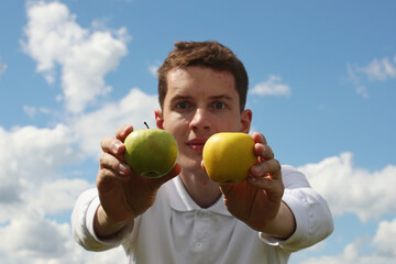 Young man with green and yellow apple on a blue sky background. Pavel Kubarkov, two apples in my hands and sky. Photo was taken 16 July 2022 year, MSK time in Russia. - 534199717