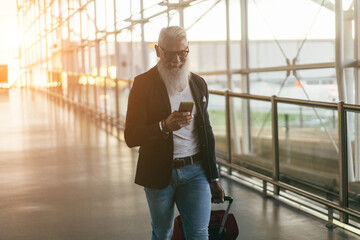 Senior business man using mobile phone inside international airport - Soft focus right hand holding...