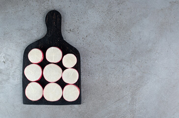 Sliced red radish on a dark board on a gray background