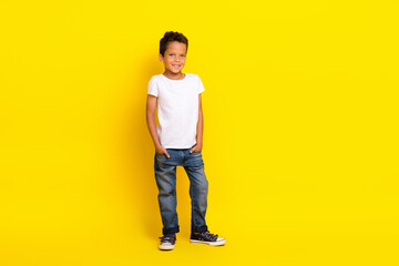 Full length photo of small boy stand wear t-shirt jeans boots isolated on yellow color background
