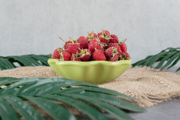 A green plate full of tasty raspberries on a sackcloth