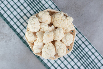 A wicker basket with uncooked cauliflower on a tablecloth
