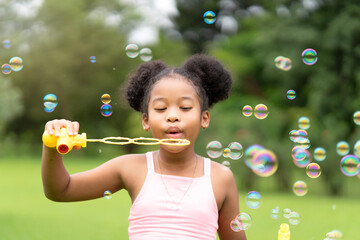 Little African American girl blowing soap bubbles in park, enjoyable to play alone with happy face.