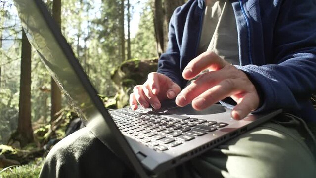Close-up of male hands making friends on a keyboard in the forest. A guy works at a computer while hiking in the mountains. A businessman solves cases on vacation. High quality 4k footage